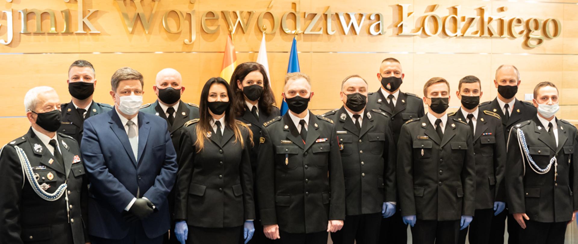 marszałek województwa łódzkiego oraz zastępca komendanta wojewódzkiego PSP w Łodzi pozujący do zdjęcia wraz z nagrodzonymi strażakami