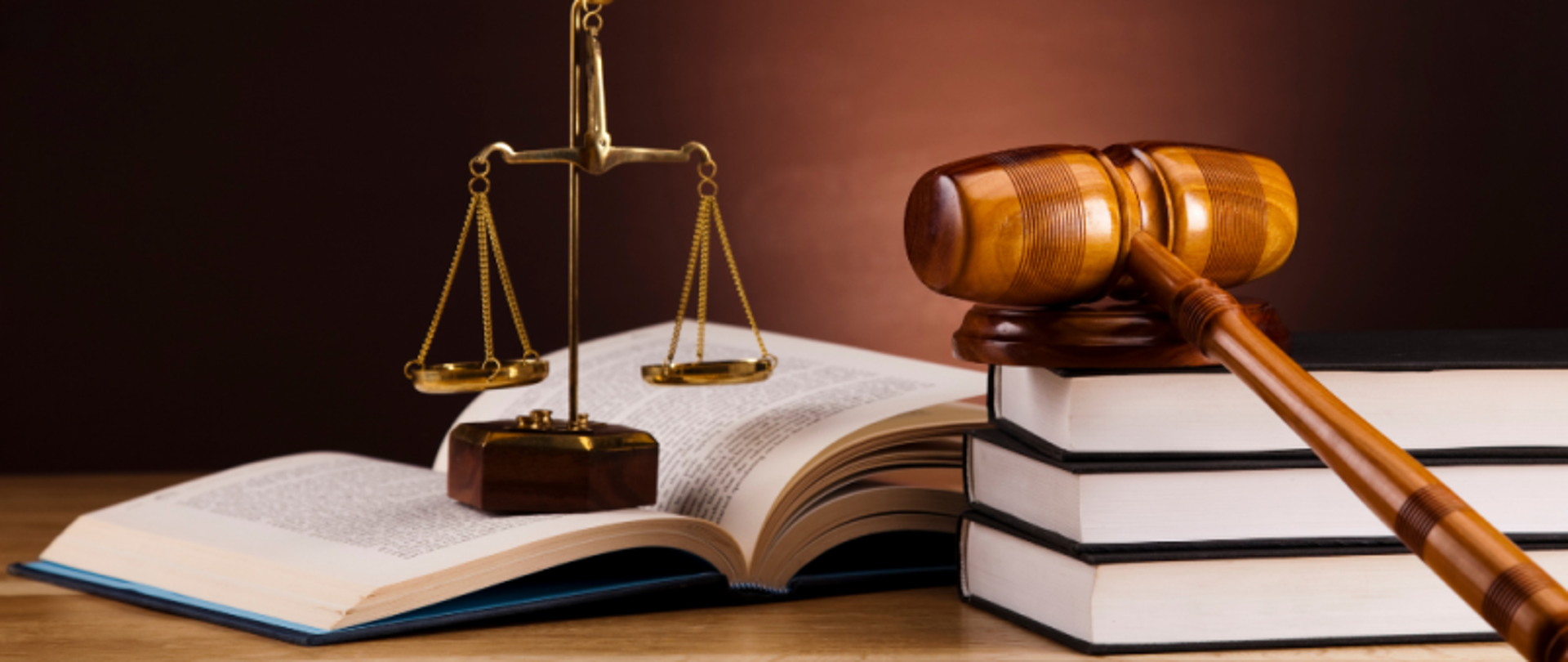 Blat biurka. Na nim leżą książki, młotek sędziowski na podstawce i ozdobna waga.