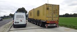 Od lewej: tył oznakowanego furgonu mazowieckiej Inspekcji Transportu Drogowego. Obok stoi ciągnik siodłowy z podpiętą naczepą dzieloną z dwoma kontenerami. Wieloosiowy i przeładowany zespół pojazdów stoi tuż za rozłożonymi wagami inspekcyjnymi w punkcie kontrolnym.