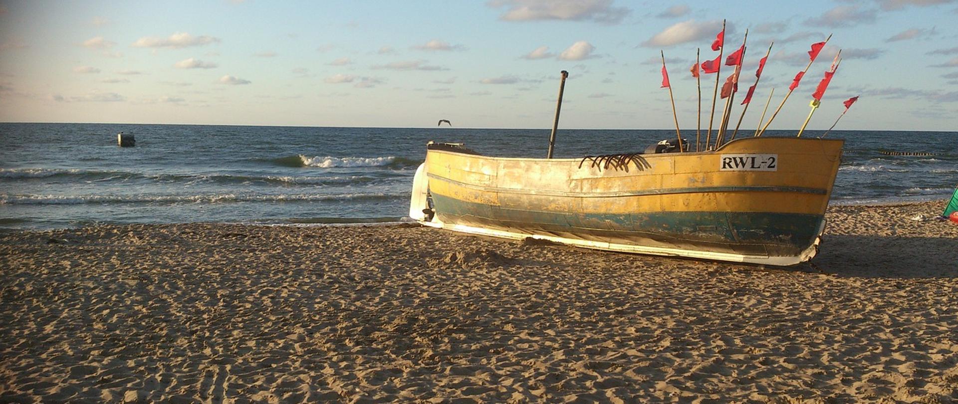 Na zdjęciu znajduje się łódź rybacka na brzegu piaszczystej plaży