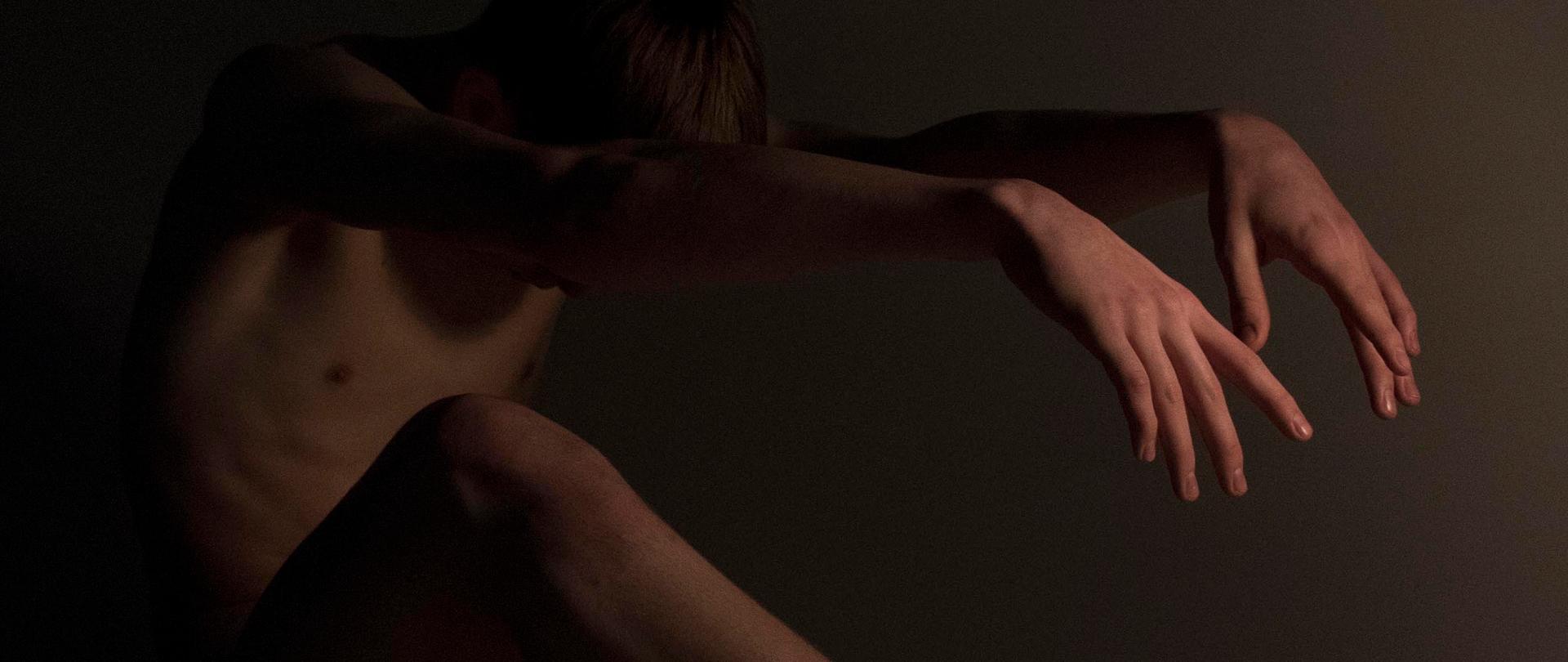 Postać młodego mężczyzny pochylona do przodu z wyprostowanymi również do przodu rękoma