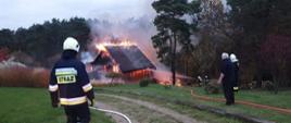 Na zdjęciu widzimy palący się dom oraz strażaków walczących z pożarem 