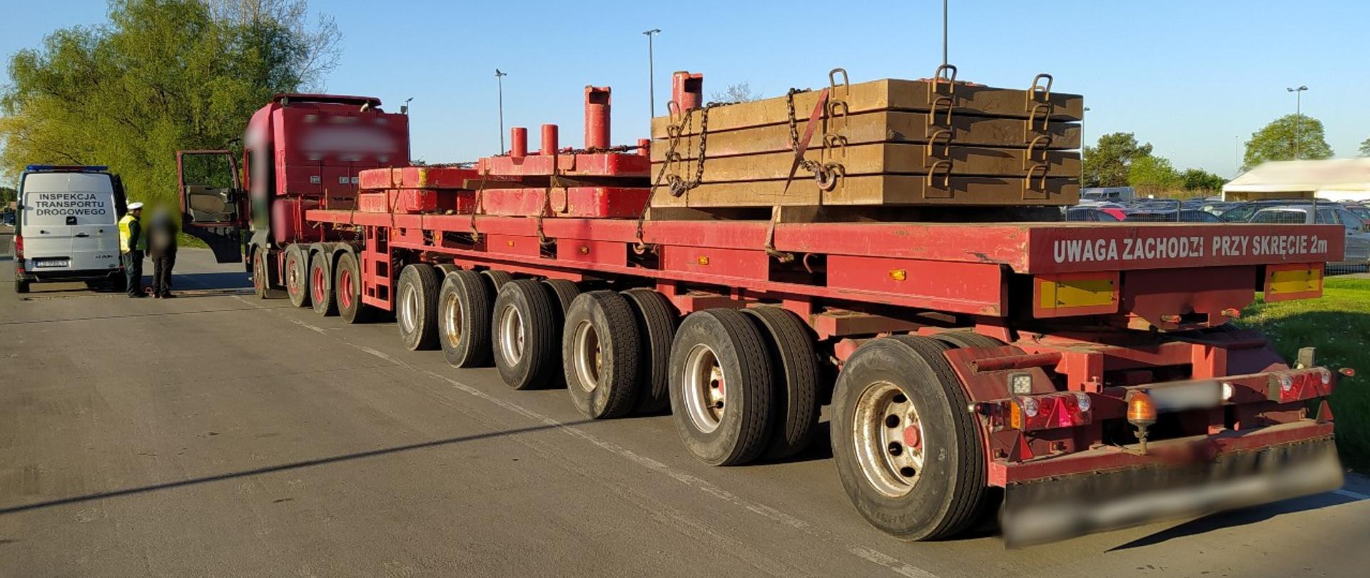 Na pierwszym planie nienormatywny zestaw z obciążeniami do dźwigu. W tle radiowóz ITD typu furgon i inspektor rozmawiający z kierowcą ciężarówki zatrzymanej do kontroli drogowej.