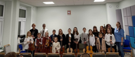 Zdjęcie przedstawia uczniów klasy gitary i skrzypiec wraz z nauczycielami. Dzieci trzymają instrumenty: skrzypce i gitary
