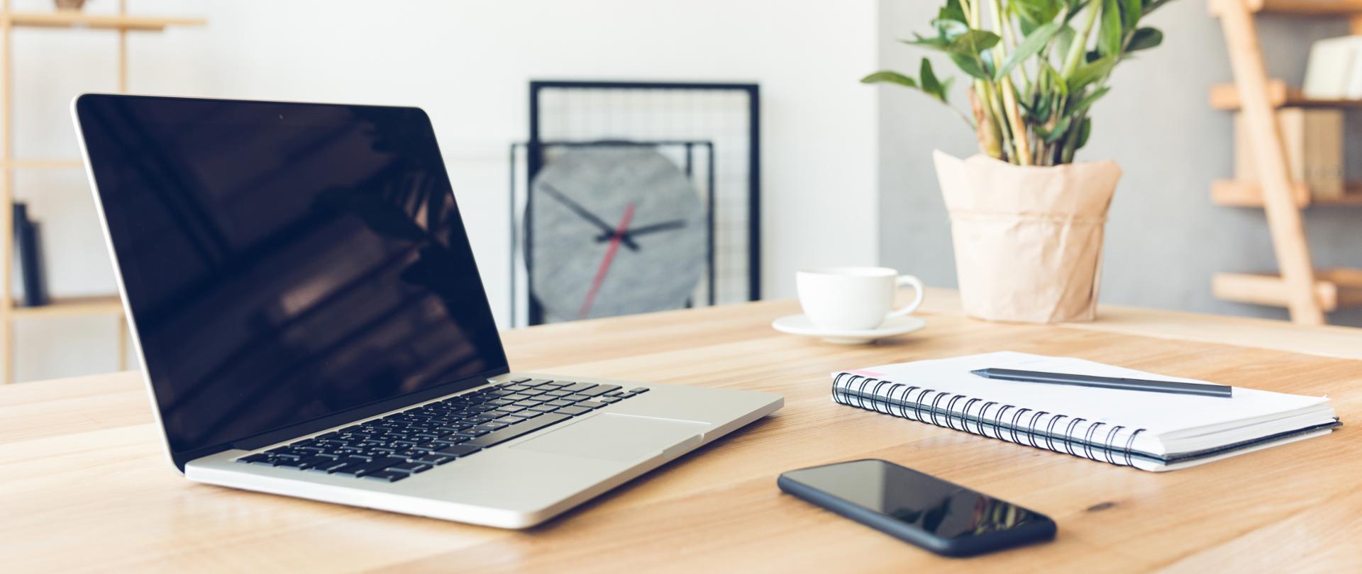 Laptop, telefon i notes na biurku a w tle kwiatek doniczkowy