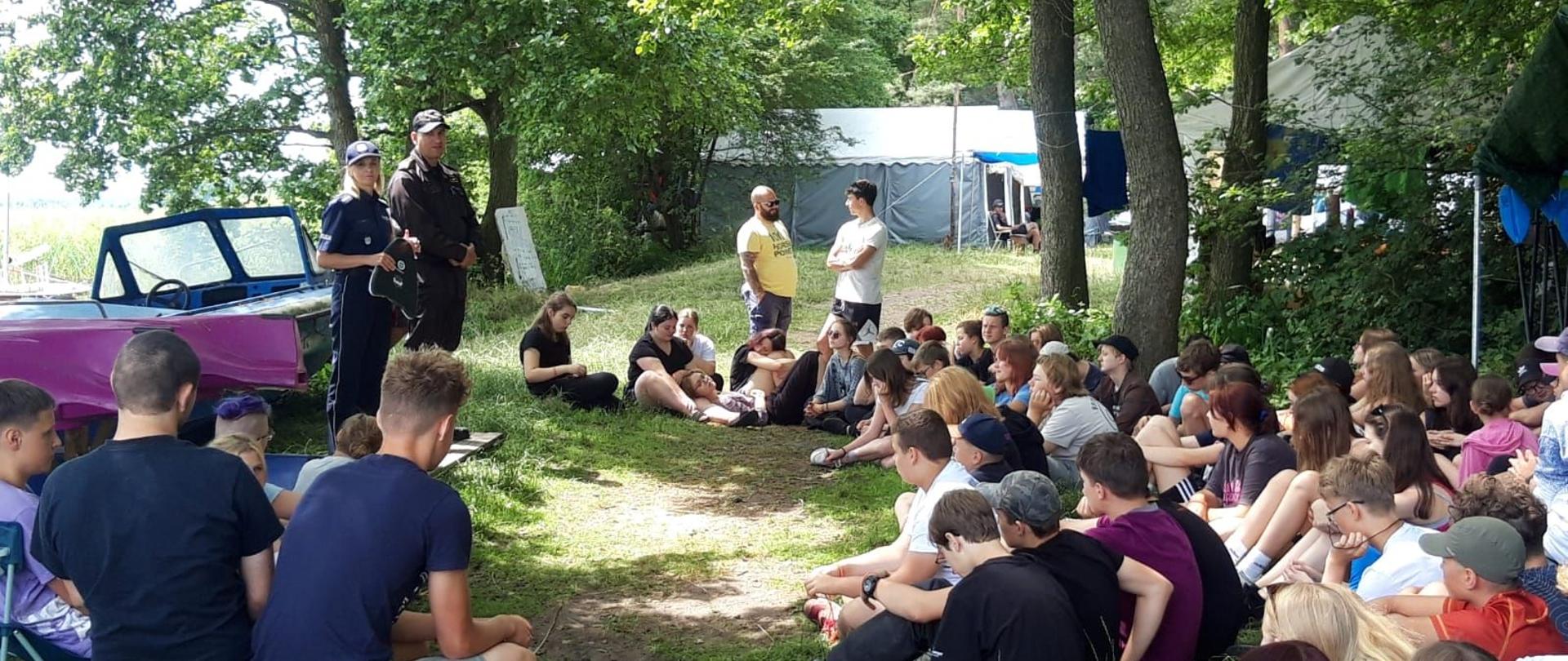 Zdjęcie przedstawia strażaka oraz policjanta podczas spotkania z młodzieżą na terenie obozu.
