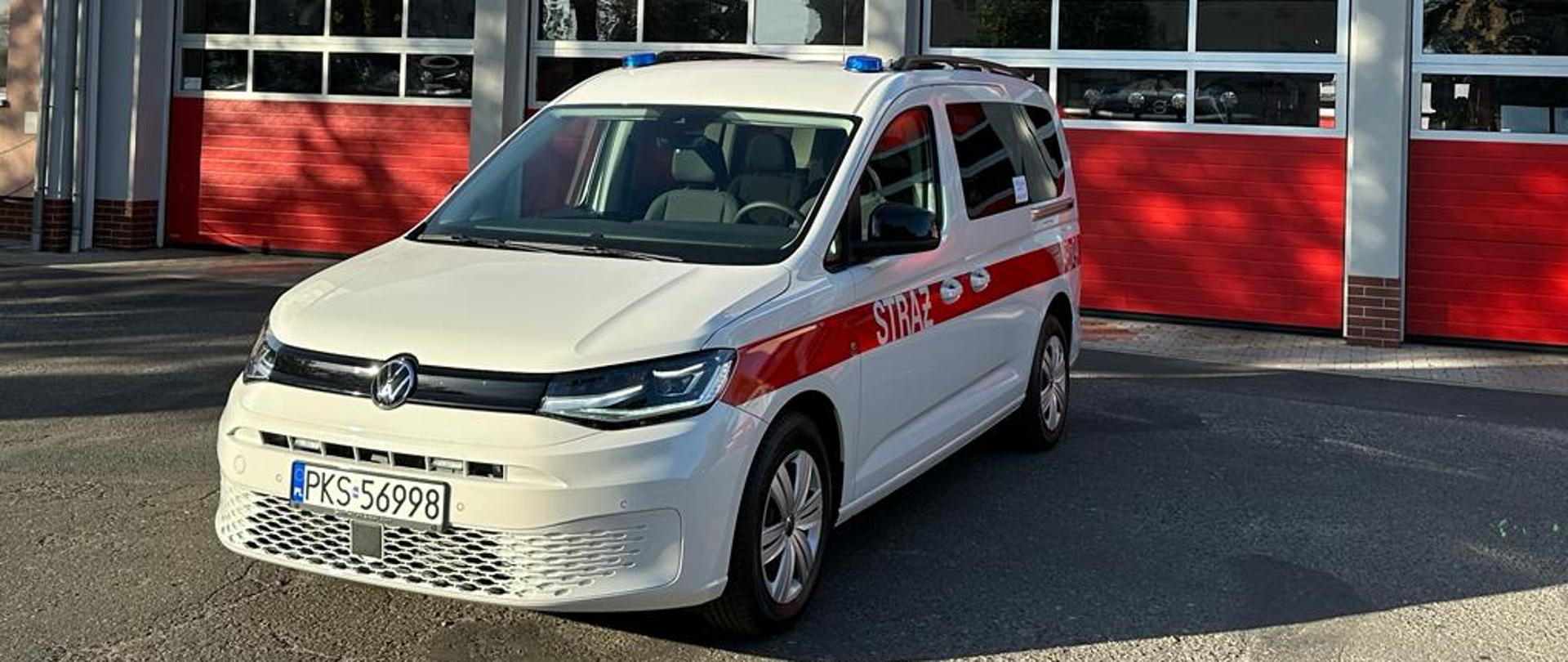 NOWY SAMOCHÓD W KOŚCIAŃSKIEJ KOMENDZIE. Na zdjęciu nowy samochód VW CADDY, biały kolor z czerwonym pasem wzdłuż pojazdu a na nim napis STRAŻ.