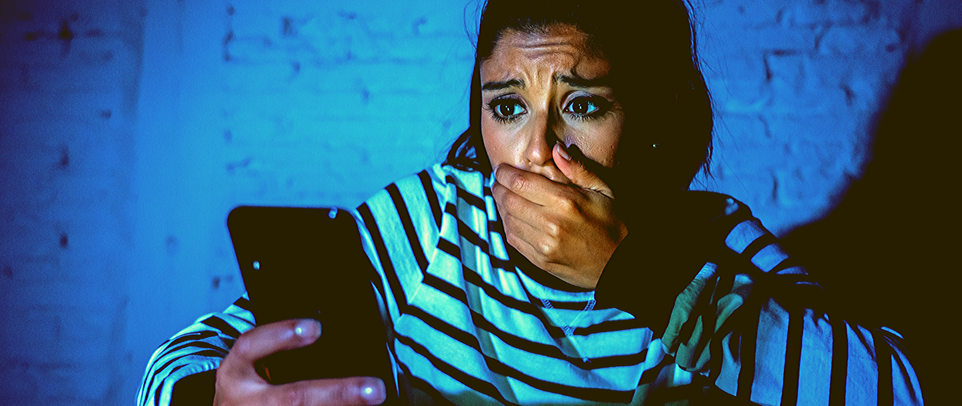 Przerażona kobieta patrzy na ekran telefonu i zakrywa usta