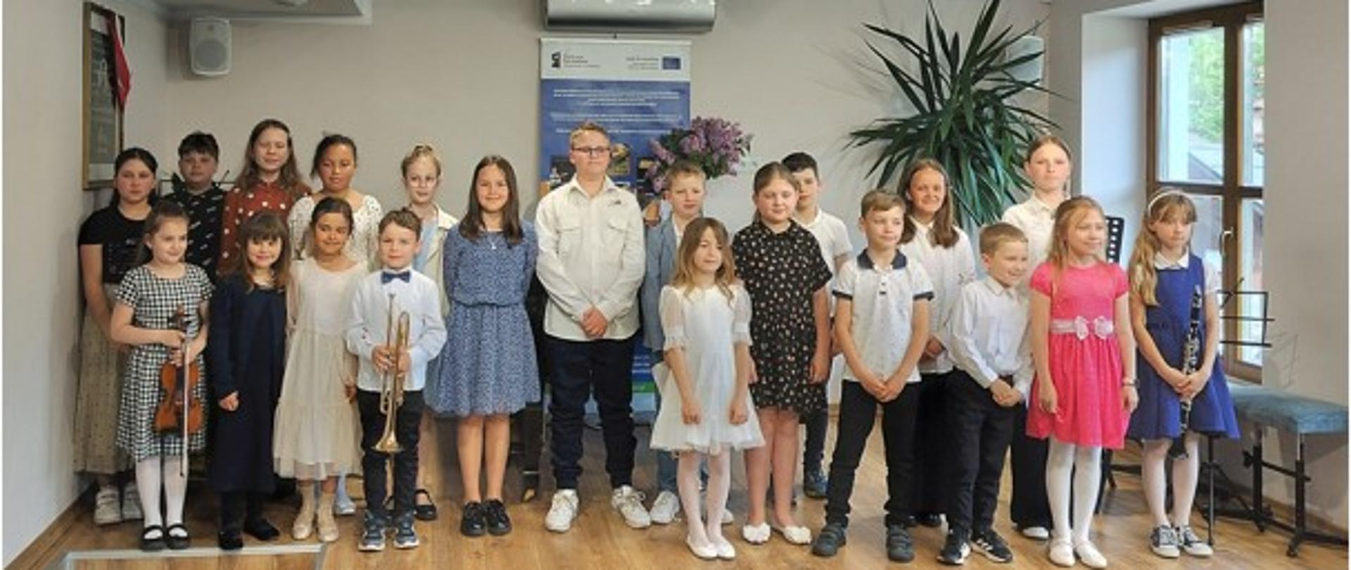 Wnętrze sali koncertowej Państwowej Szkoły Muzycznej I i II stopnia im. Fryderyka Chopina w Nowym Targu - filia w Jaworkach.
Na pierwszym planie uczniowie stojący na podwyższeniu sceny uczniowie biorący udział w koncercie z okazji Dnia Matki. Kilkoro trzyma w ręce instrumenty.