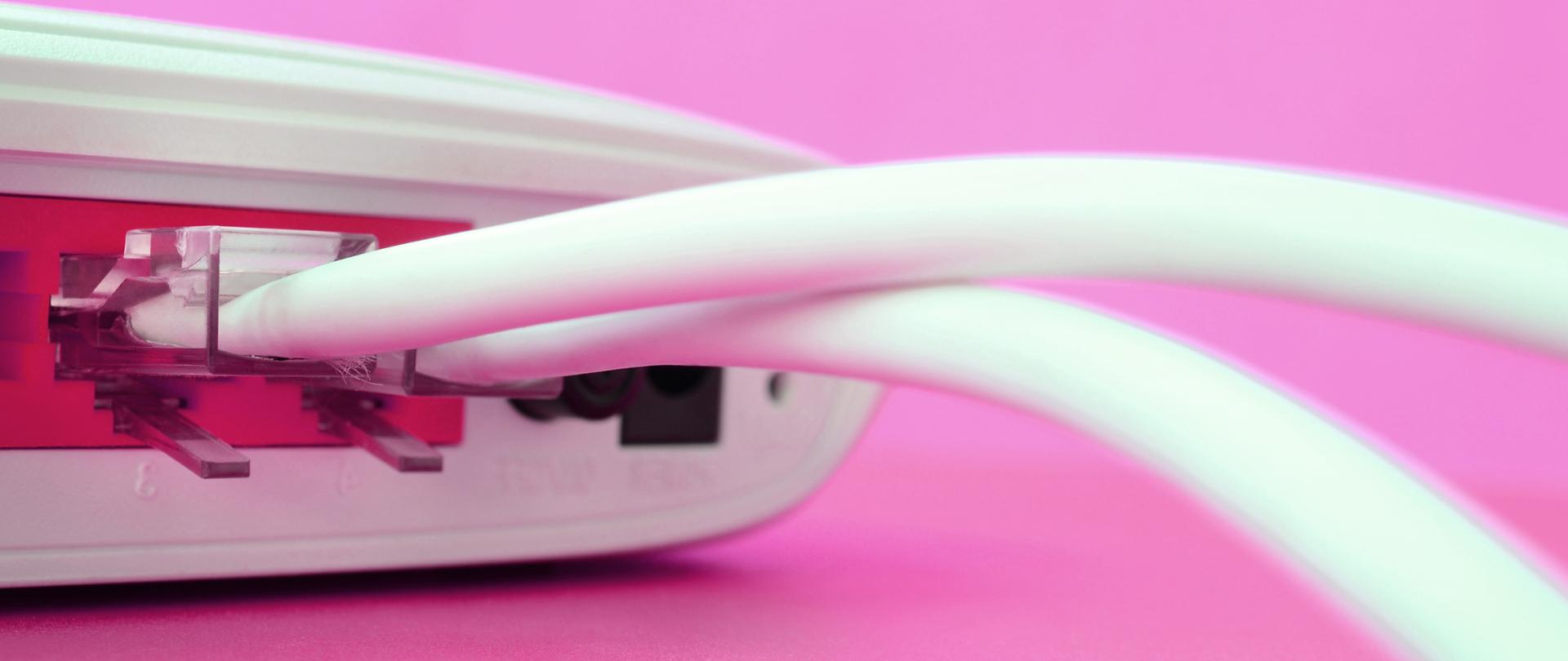 Na różowym tle zdjęcie białego kabla podłączonego do modemu.