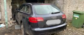 Zdjęcie przedstawia czarne auto typu kombi, które wjechało w ścianę burząc ją częściowo.