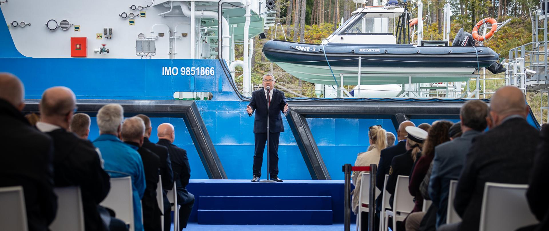 Minister infrastruktury Andrzej Adamczyk na tle statku Zodiak II w trakcie otwarcia Kanału żeglugowego przez Mierzeję Wiślaną