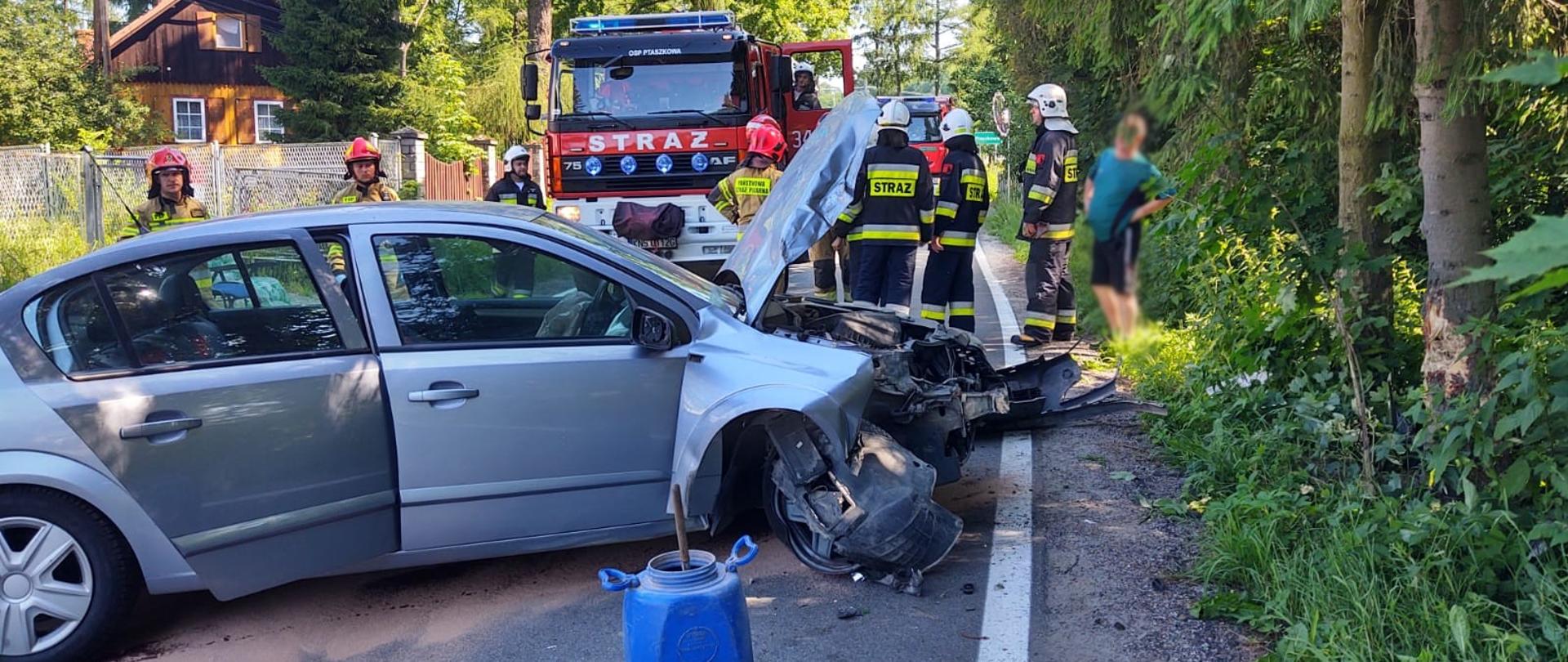 Samochód osobowy stoi w poprzek drogi. Za nim strażacy oraz samochody pożarnicze.