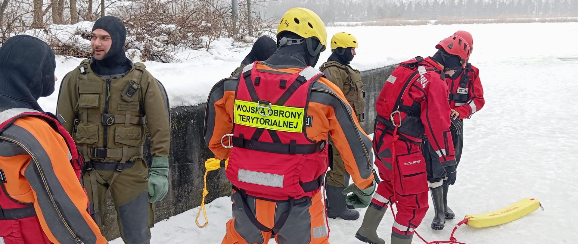 Funkcjonariusze ubrani w kombinezony prowadzą ćwiczenia na lodzie rzeki