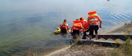 na zdjęciu widzimy strażaków w kamizelkach ratunkowych ćwiczących podejmowanie osoby poszkodowanej z wody