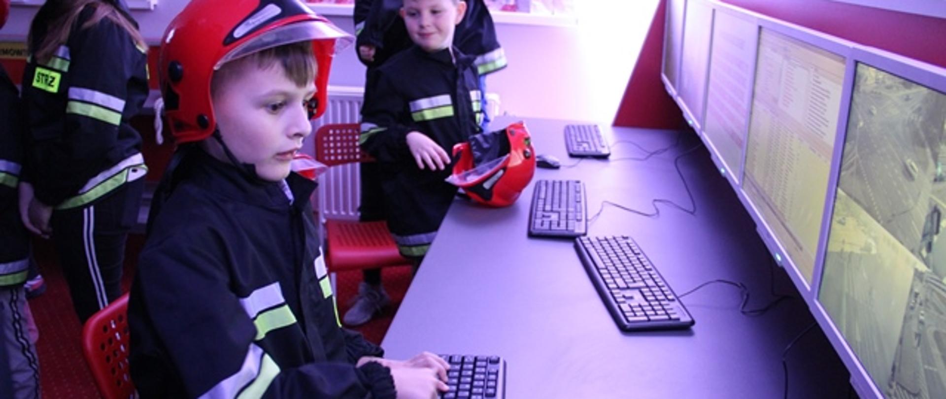 Na zdjęciu dzieci podczas zajęć w salce edukacyjnej w strażnicy w Grudziądzu. Chłopiec operuje monitoringiem wizyjnym podczas lokalizacji interweniującej jednostki.
