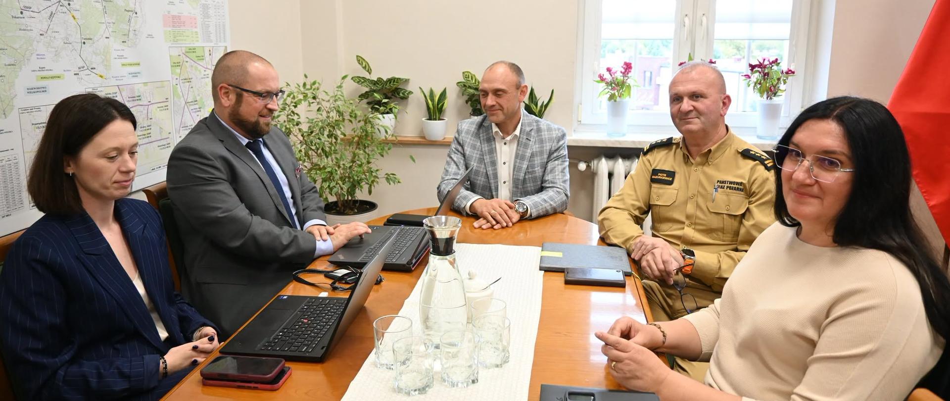 Uczestnicy spotkania siedzą przy stole w gabinecie.