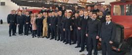 Zdjęcie grupowe uczestników warsztatów, za nimi widoczne są zabytkowe wozy gaśnicze straży pożarnej