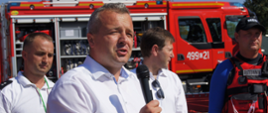 wojewoda Mikołaj Bogdanowicz mówi do mikrofonu, w tle wóz strażacki