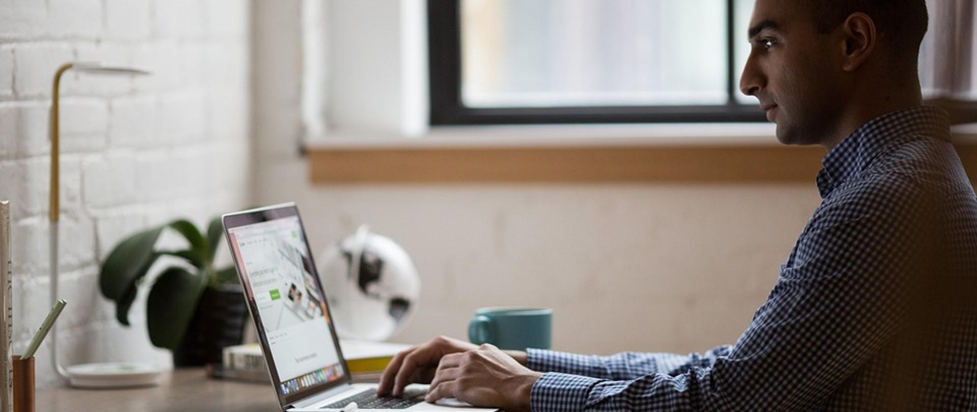 Mężczyzna siedzący przed laptopem, na którym pracuje.