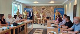 Zdjęcie z zakończenia szkolenia. Na pierwszym planie po bokach przy stołach urzędnicy patrzą w stroną drugoplanowego Komendanta Wojewódzkiego, który stoi i przemawia. Obok starosta i inni oficerowie.