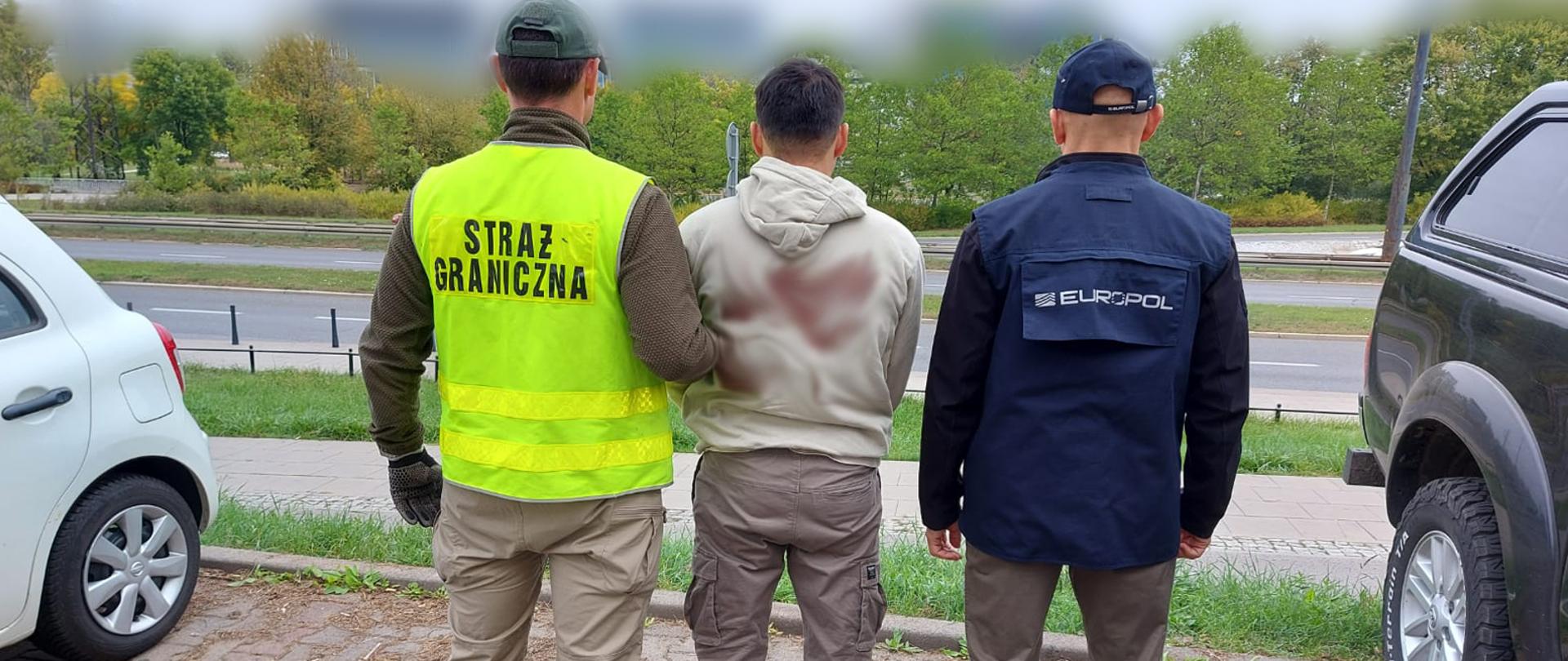 Zdjęcie przedstawia funkcjonariuszy służb Straży Granicznej i Eurlopolu z osobą zatrzymaną w ramach prowadzonych śledztw