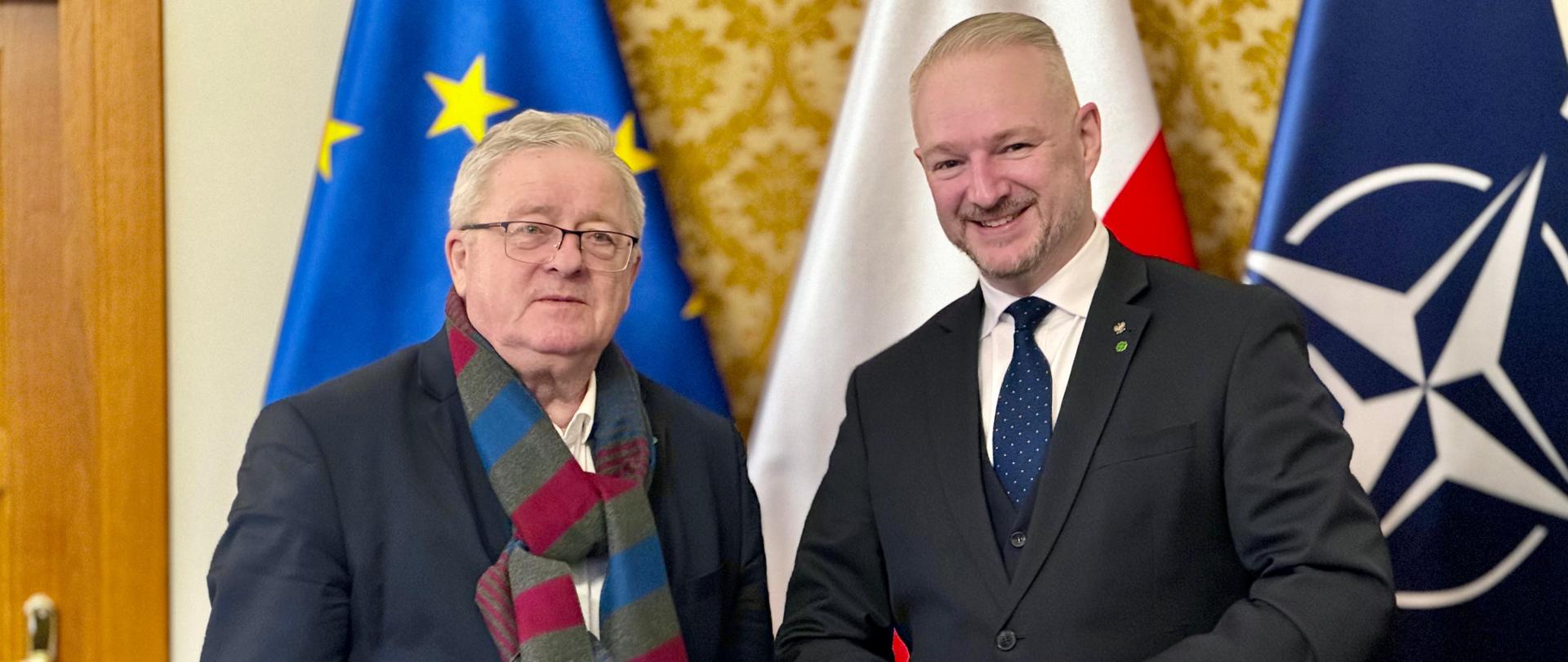 Czesław Siekierski – Minister Rolnictwa i Rozwoju Wsi podczas spotkania w 10 stycznia 2025 r. z Wojewodą Warmińsko-Mazurskim Radosławem Król. Dwa mężczyźni pozują do pamiątkowej fotografii na tle flag w gabinecie wojewody.