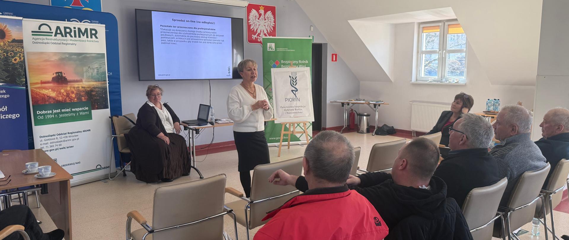 Uczestnicy spotkania siedzący na sali konferencyjnej wraz z prelegentem.