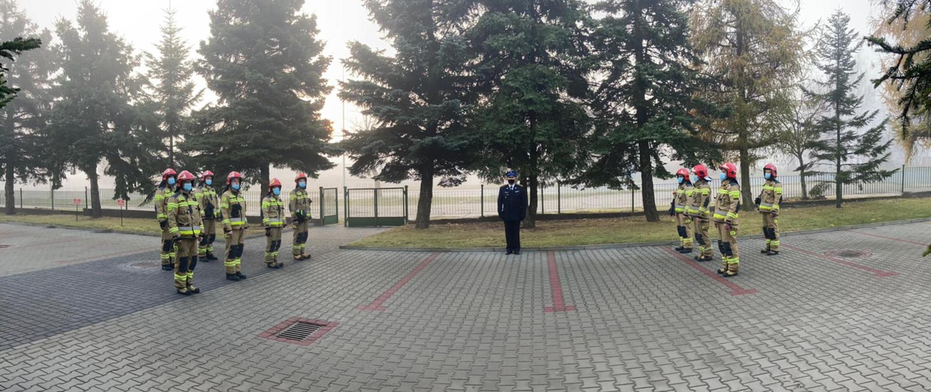 Na zdjęciu uroczysta zmiana służby. Zastępca dowódcy jednostki w umundurowaniu galowym prowadzi uroczystość. Na zdjęciu widoczni strażacy w ubraniu bojowym stojący po prawej i lewej stronie. 