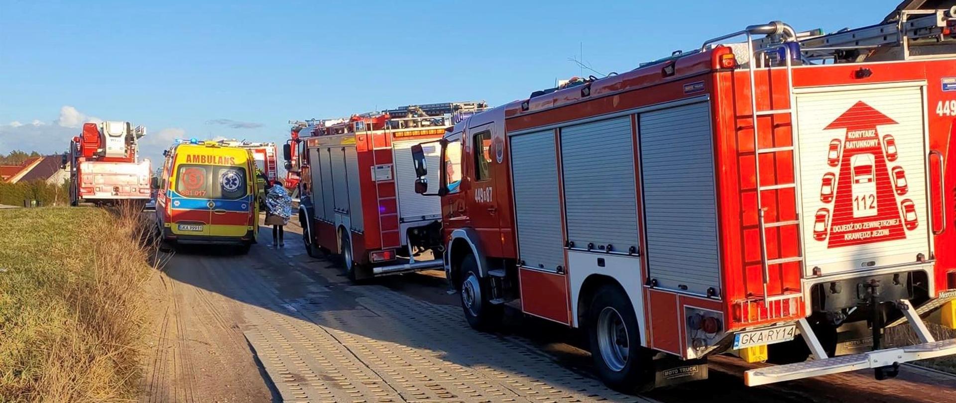 Samochody służb ratowniczych ustawione na drodze w pobliżu miejsca pożaru.