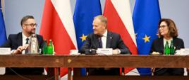 Za stołem siedzą minister Kulasek, premier Tusk i marszałek Kidawa-Błońska, za nimi szereg flag Polski i UE.