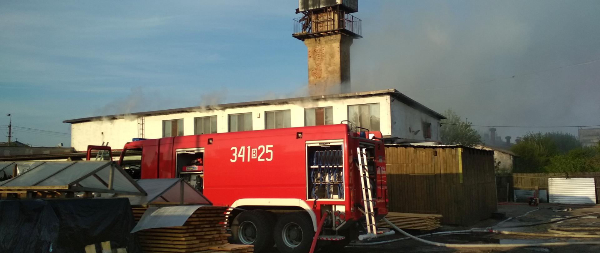 Zdjęcie wykonane od strony wjazdu na posesję. Widać ciężki samochód pożarniczy, rozwinięte węże w stronę budynku stolarni.