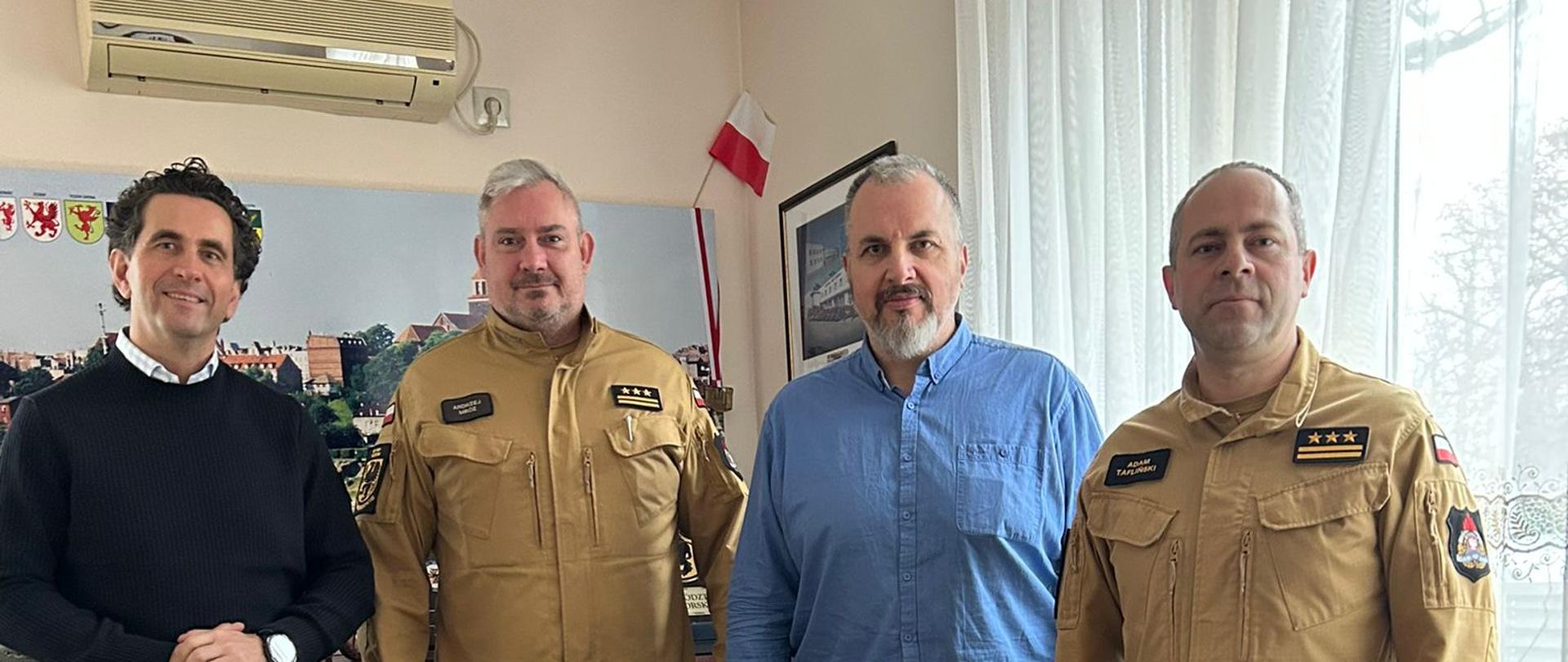 Czterech mężczyzn - w tym dwóch w mundurach (komendant i zastępca) podczas wspólnego zdjęcia, przed nimi karton z kokardą.