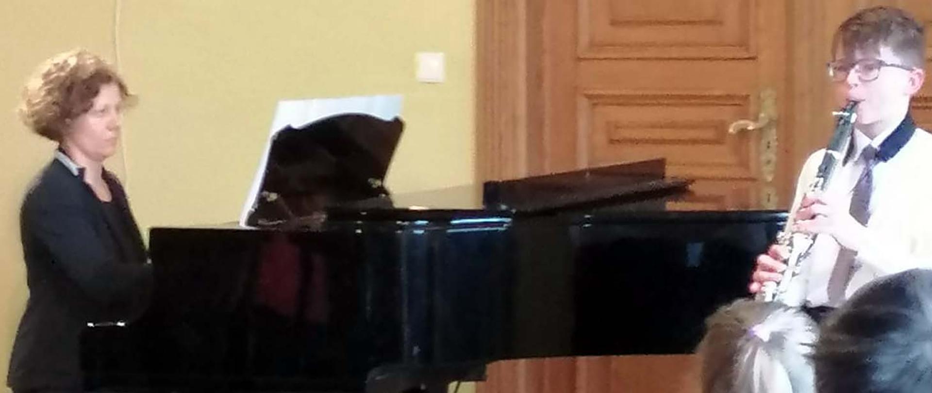 Ignacy Homziuk gra na klarnecie w towarzystwie kobiety akompaniującej mu na fortepianie.