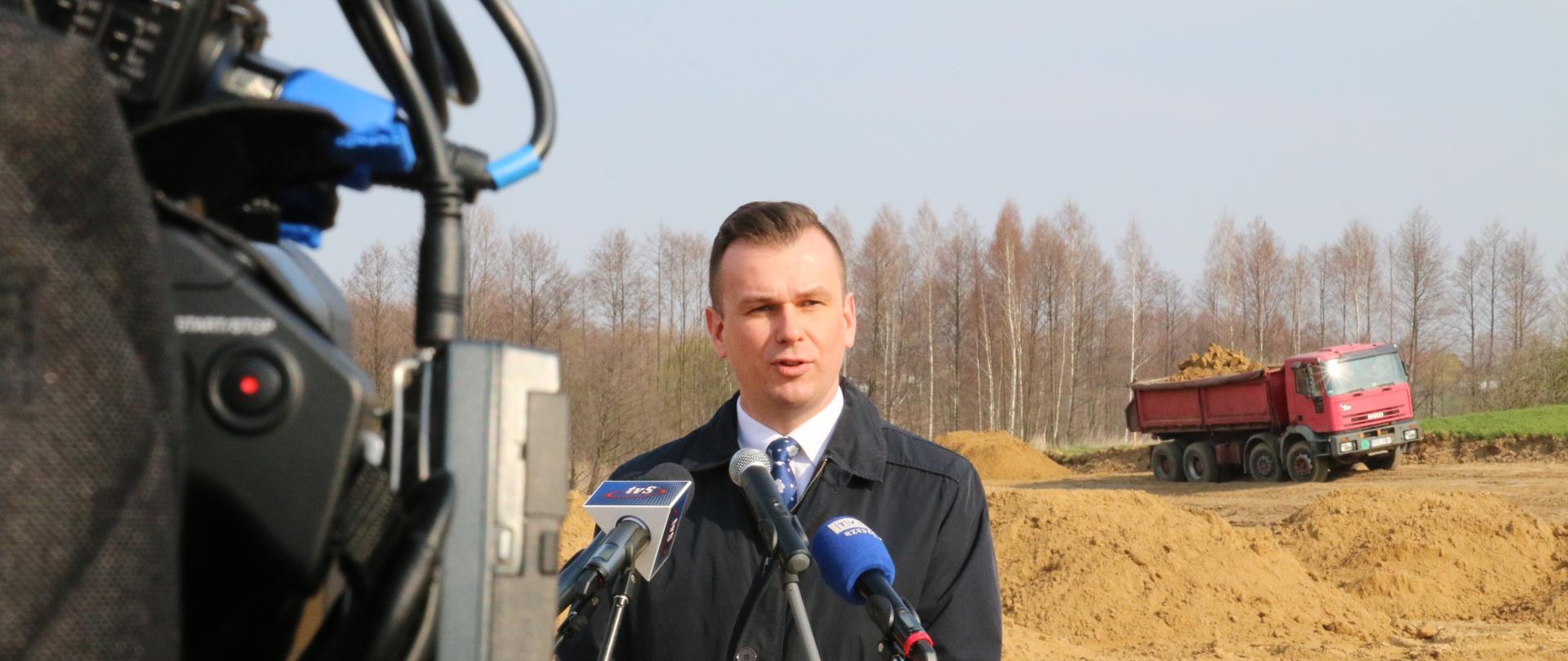 Na tle budowy drogi wiceminister Adam Hamryszczak przemawia do mikofonu