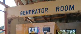 Widać duże metalowe urządzenia, na górze napis Generator Room, z tyłu okno przez które widać palmy
