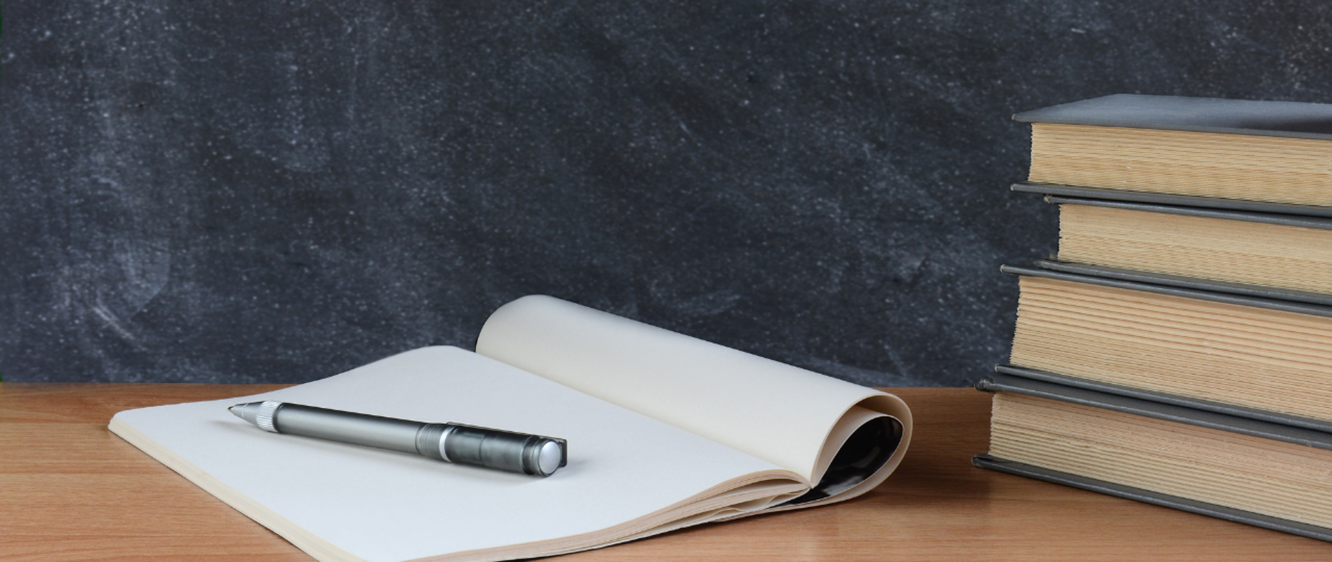 Na blacie leży stos książek, obok zeszyt z piórem 