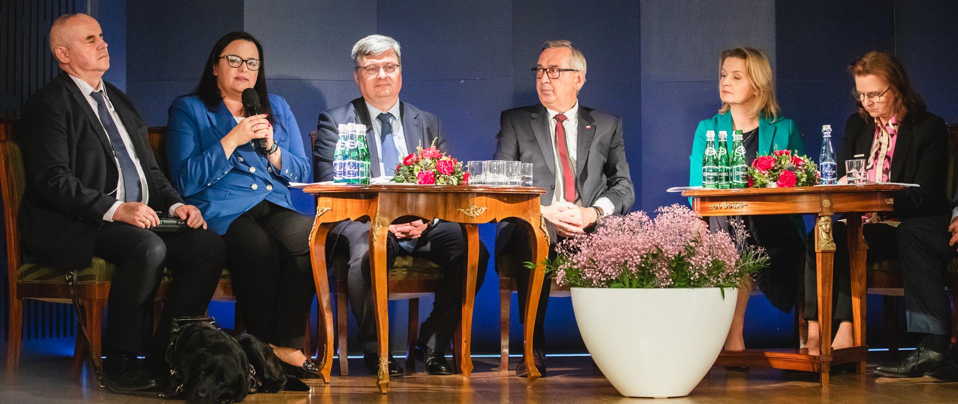 Grupa osób siedzi przy stolikach. Druga od lewej wiceminister Małgorzata Jarosińska-Jedynak z mikrofonem.