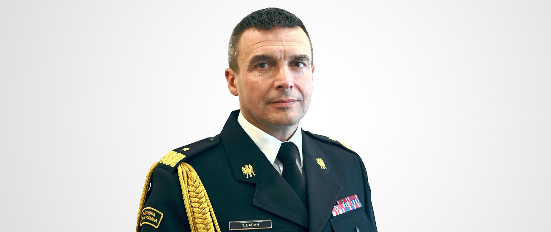 Na jasnym tle zdjęcie portretowe Podkarpackiego Komendanta Wojewódzkiego PSP nadbryg. Tomasza Barana w mundurze galowym
