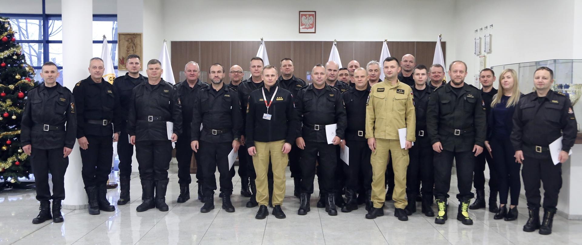 Grupowe zdjęcie uczestników szkolenia (19 funkcjonariuszy PSP) w towarzystwie Zastępcy Komendanta Centralnej Szkoły PSP, trzech funkcjonariuszy CS PSP i kobiety