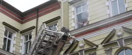 Na zdjęciu widać kobietę stojącą przy oknie na II piętrze budynku starostwa powiatowego w Jarosławiu, która wzywa pomocy. Z okna wydobywa się dym. Na pierwszym planie widać również rozkładającą się drabinę mechaniczną.