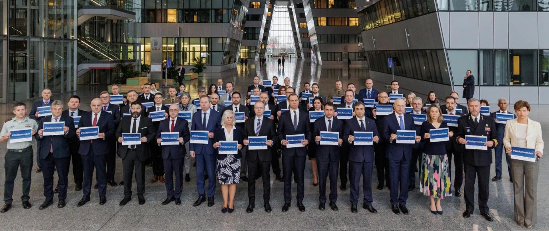 Ambasadorowie przy NATO z kartkami z napisem "we remember"