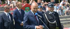 XI Powiatowe Zawody Sportowo-Pożarnicze OSP i MDP. Stadion w Miejskiej Górce. Na tle gości, komisji sędziowskiej i trybun, na których zasiadają kibice, do zebranych przemawia starosta rawicki. 