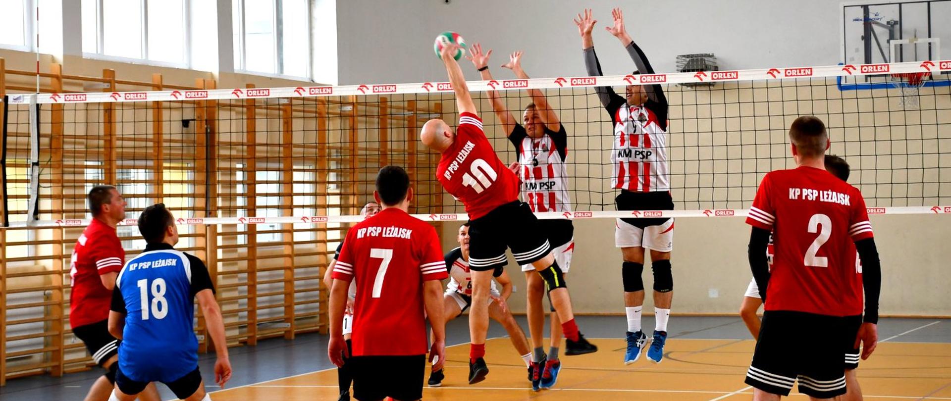 Zdjęcie zrobione w hali sportowej. Zawodnicy rozgrywają mecz piłki siatkowej.