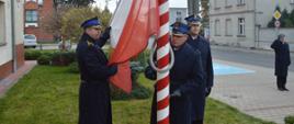 Narodowe Święto Niepodległości. Plac przed Komendą Powiatową PSP w Rawiczu. Poczet flagowy. podnosi flagę państwową na maszt. W tle budynki i drzewa.