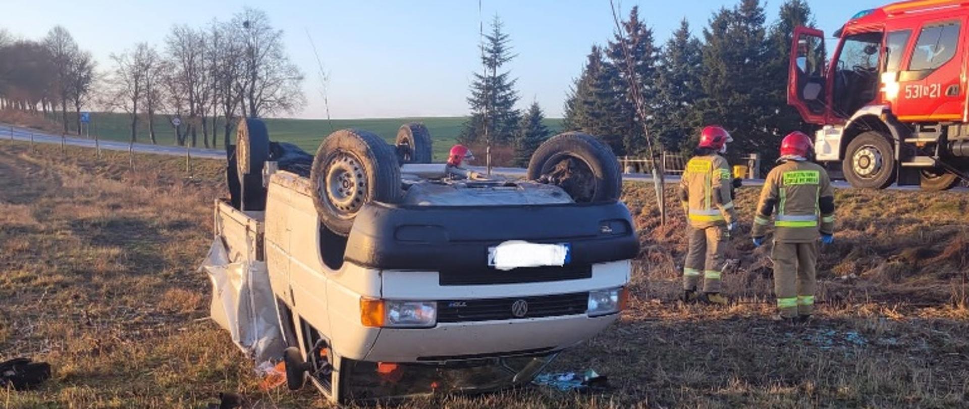 Samochód dostawczy leży na dachu po wypadnięciu z drogi. 