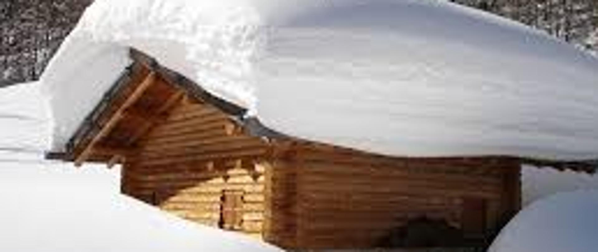 Zdjęcie przedstawia drewnianą chatę z kilkudziesięcio cenymetrową pokrywą śniegu.