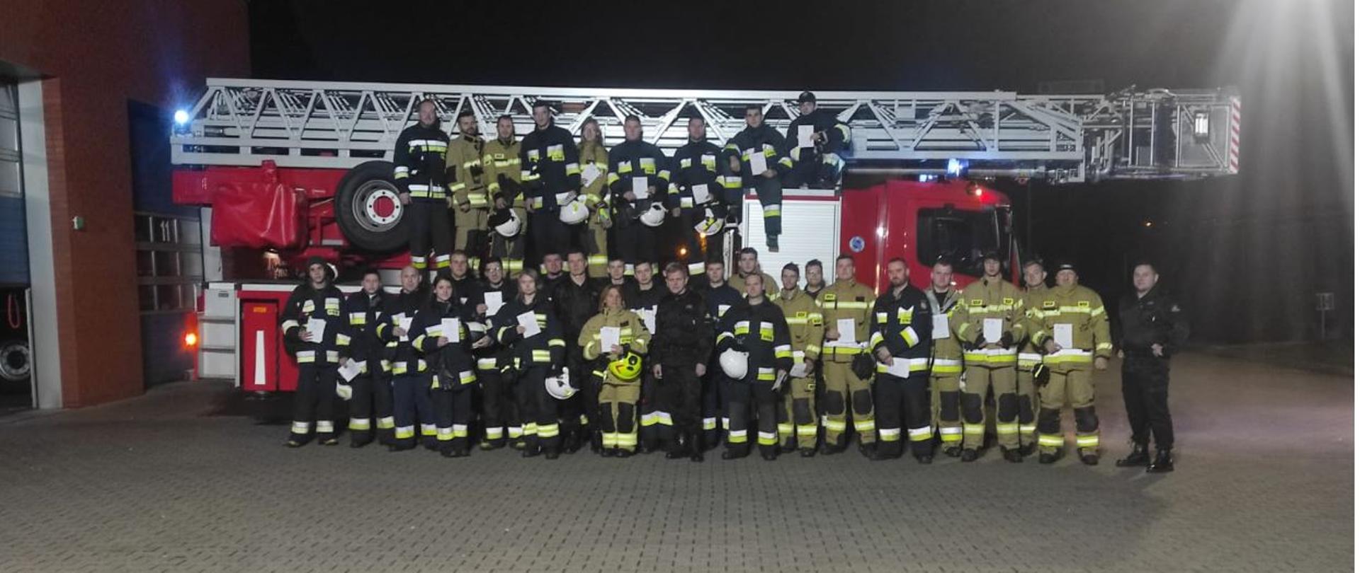 grupa strażaków przed wozem bojowym