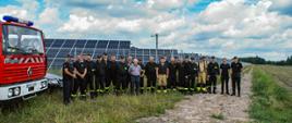 Zdjęcie pamiątkowe na tle pojazdów pożarniczych i paneli fotowoltaicznych. Na zdjęciu uczestniczący w rozpoznaniu strażacy i wykonawca instalacji. 