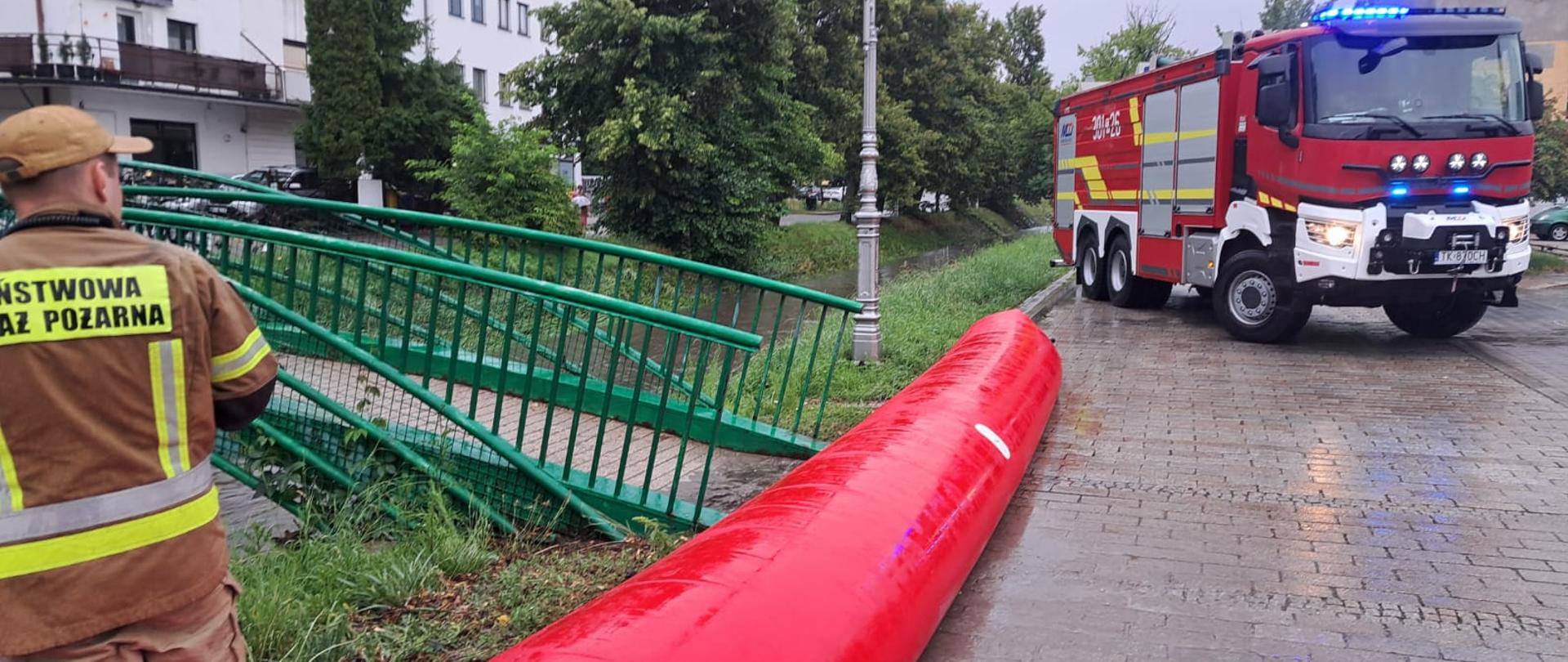 Zdjęcie przedstawia ulicę Planty w Kielcach: po lewej stronę rękawy przeciwpowodziowe, a w głębi samochód pożarniczy blokujący wjazd.